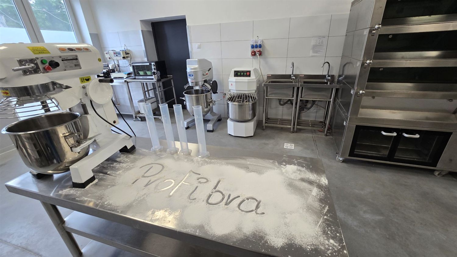 Napis ProFibra wypisany w mące na stalowym stole w pracowni piekarniczej